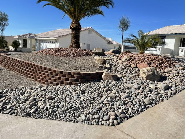 Block retaining wall with river rock, boulders and a trimmed palm